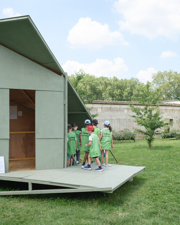 Un groupe de jeunes enfants visitant une structure en bois peint en vert dans les jardins de Versailles.