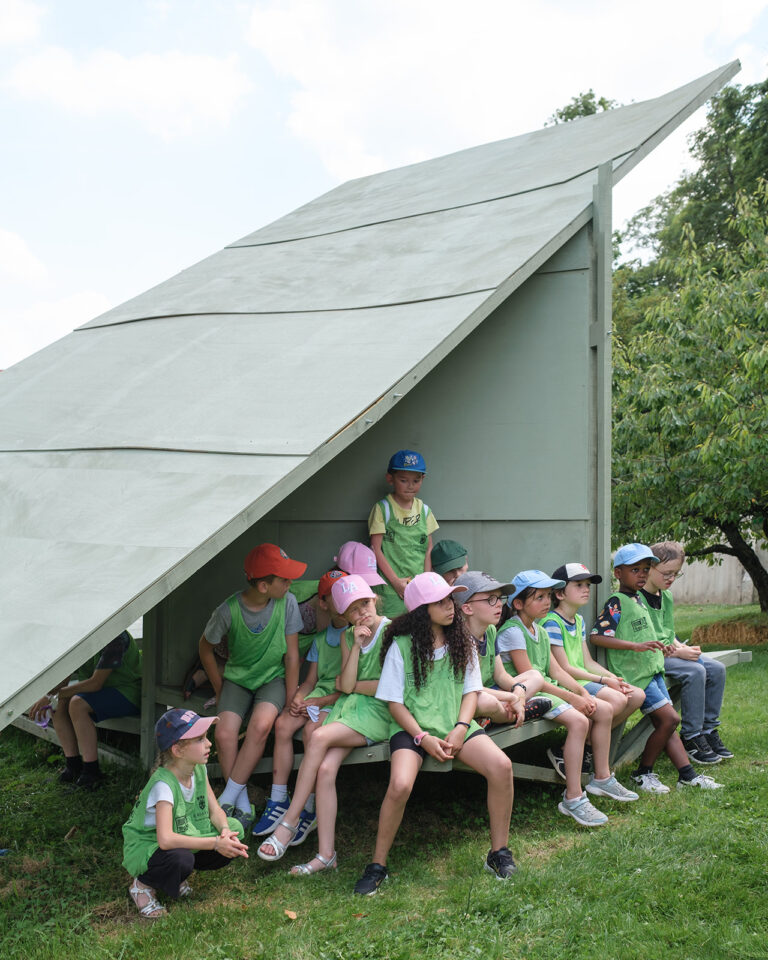 Un groupe de jeunes enfants assis sur une structure en bois peint en vert dans les jardins de Versailles.