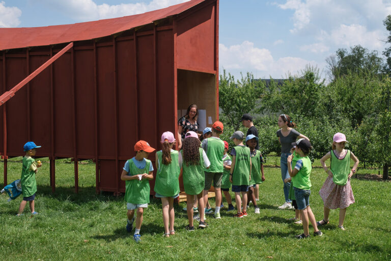 Groupe de jeunes enfants se trouvant dans les jardins de Versailles, observant une structure en bois rouge.