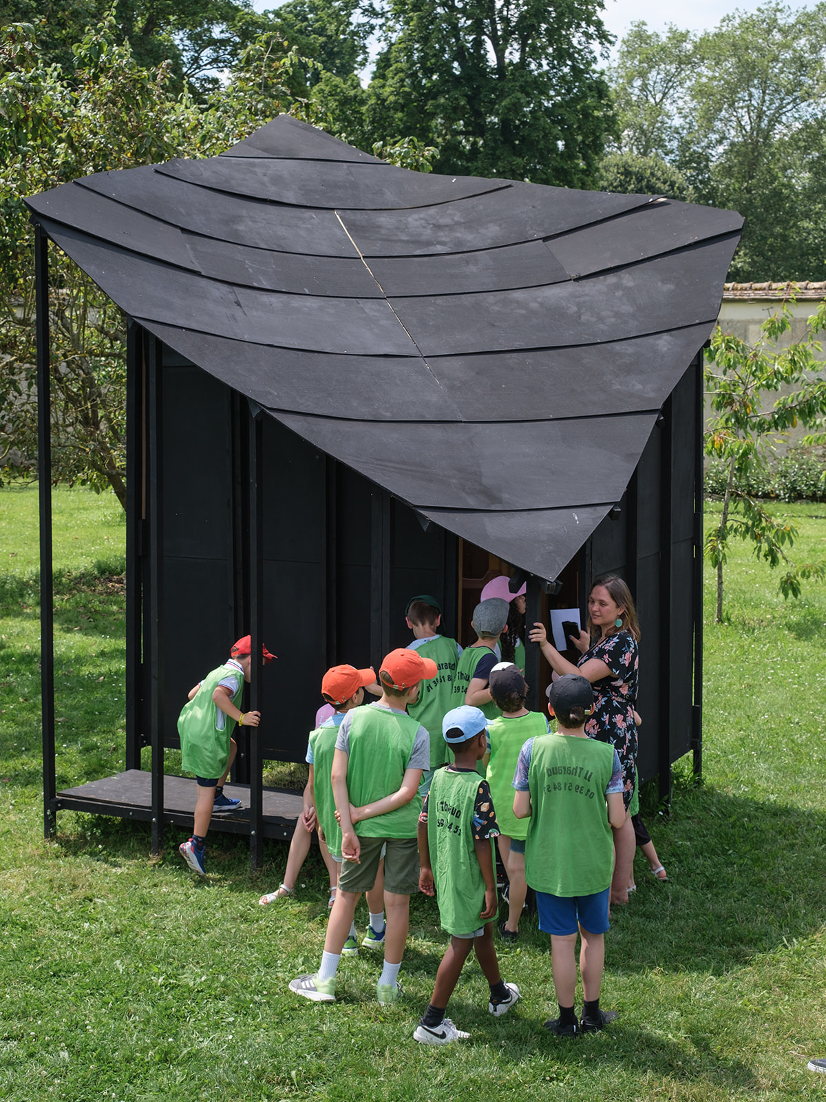 Groupe de jeunes enfants se trouvant dans les jardins de Versailles, observant une structure en bois noir.
