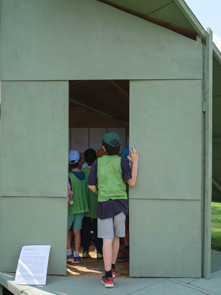 Un groupe de jeunes enfants visitant une structure en bois peint en vert dans les jardins de Versailles.