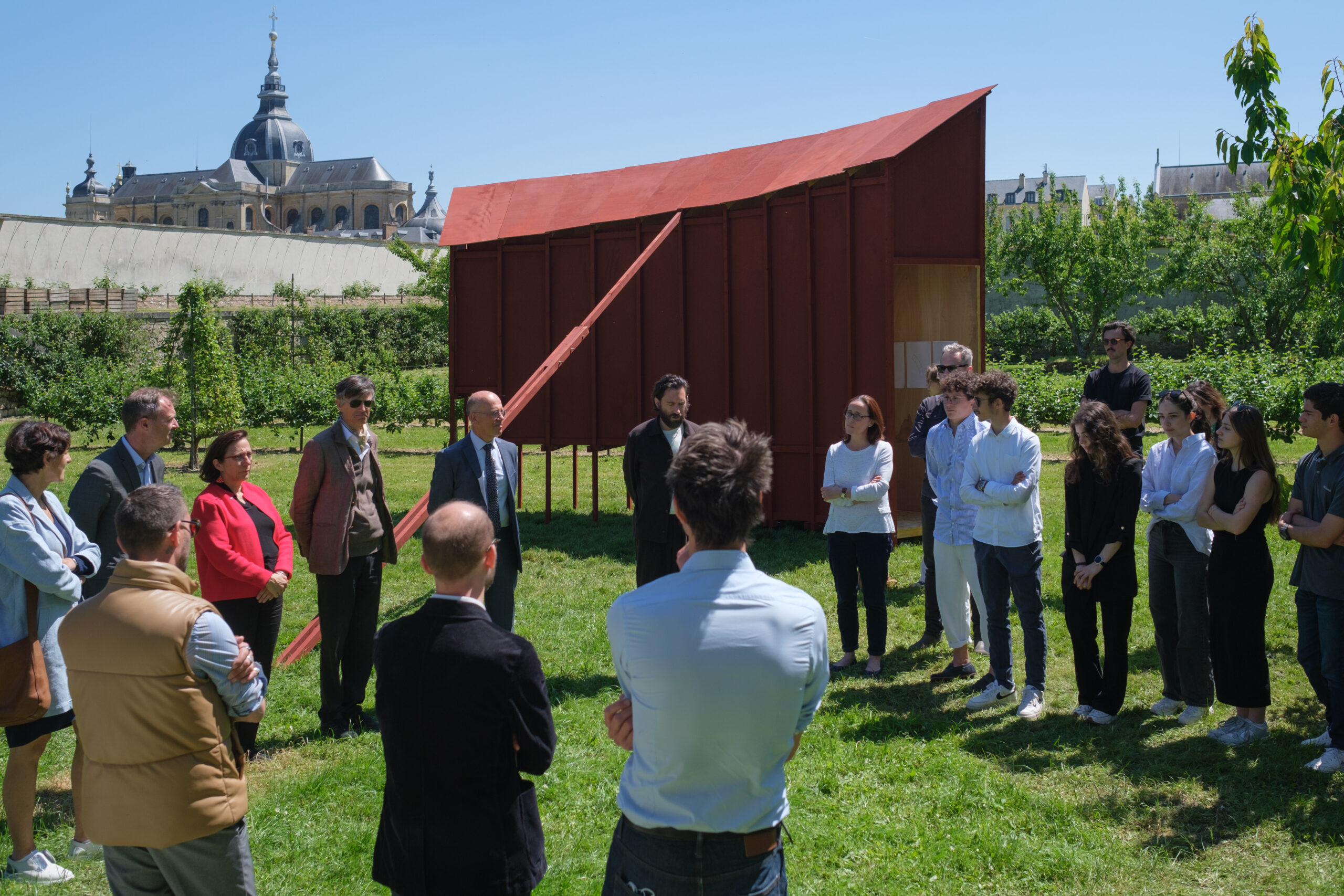 Groupe de personne discutant, structure en bois peint en rouge au second plan, châteaux de Versailles en fonds